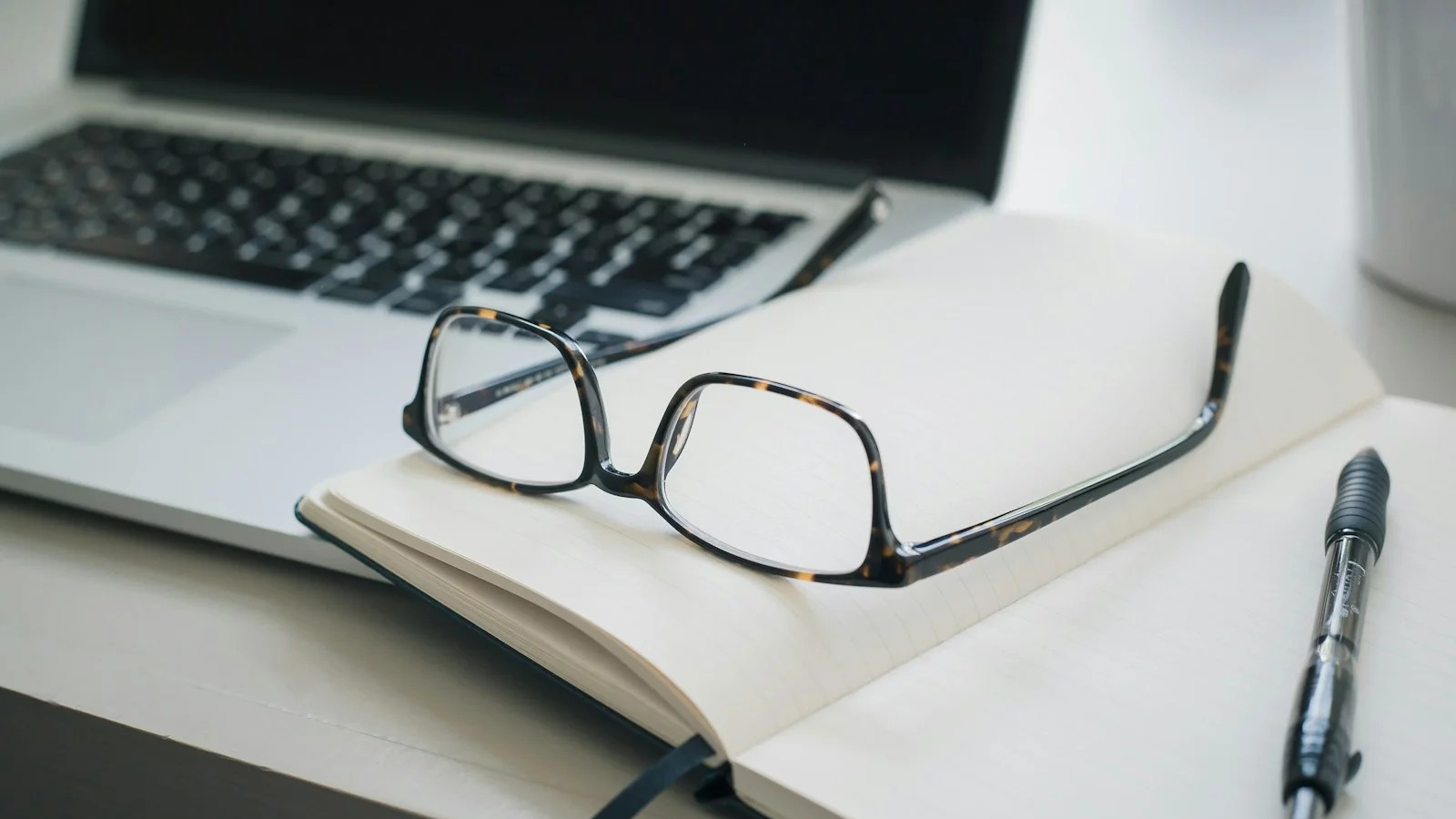 Lunettes sur carnet, ordinateur portable et stylo dans un bureau moderne.